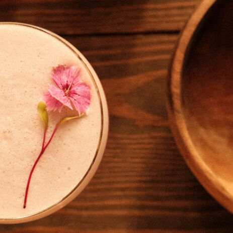 Cocktail crémeux décoré d'une fleur rose sur table en bois, carte des cocktails d'AZULIK I INLA