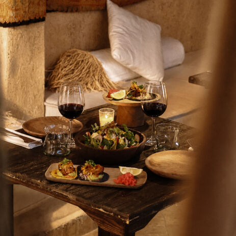 Table dressée avec plats et verres de vin rouge sur banquette, dîner chez AZULIK I INLA, Marrakech