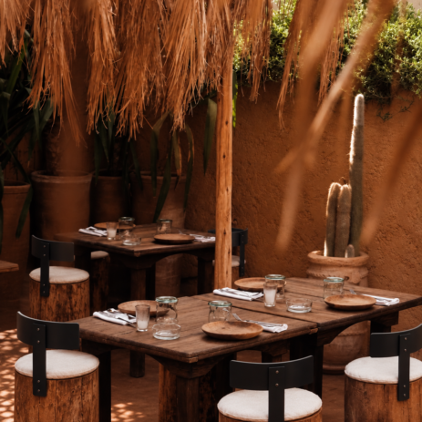 Tables en bois et tabourets en tronc sous les palmes séchées, patio d'AZULIK I INLA à Marrakech
