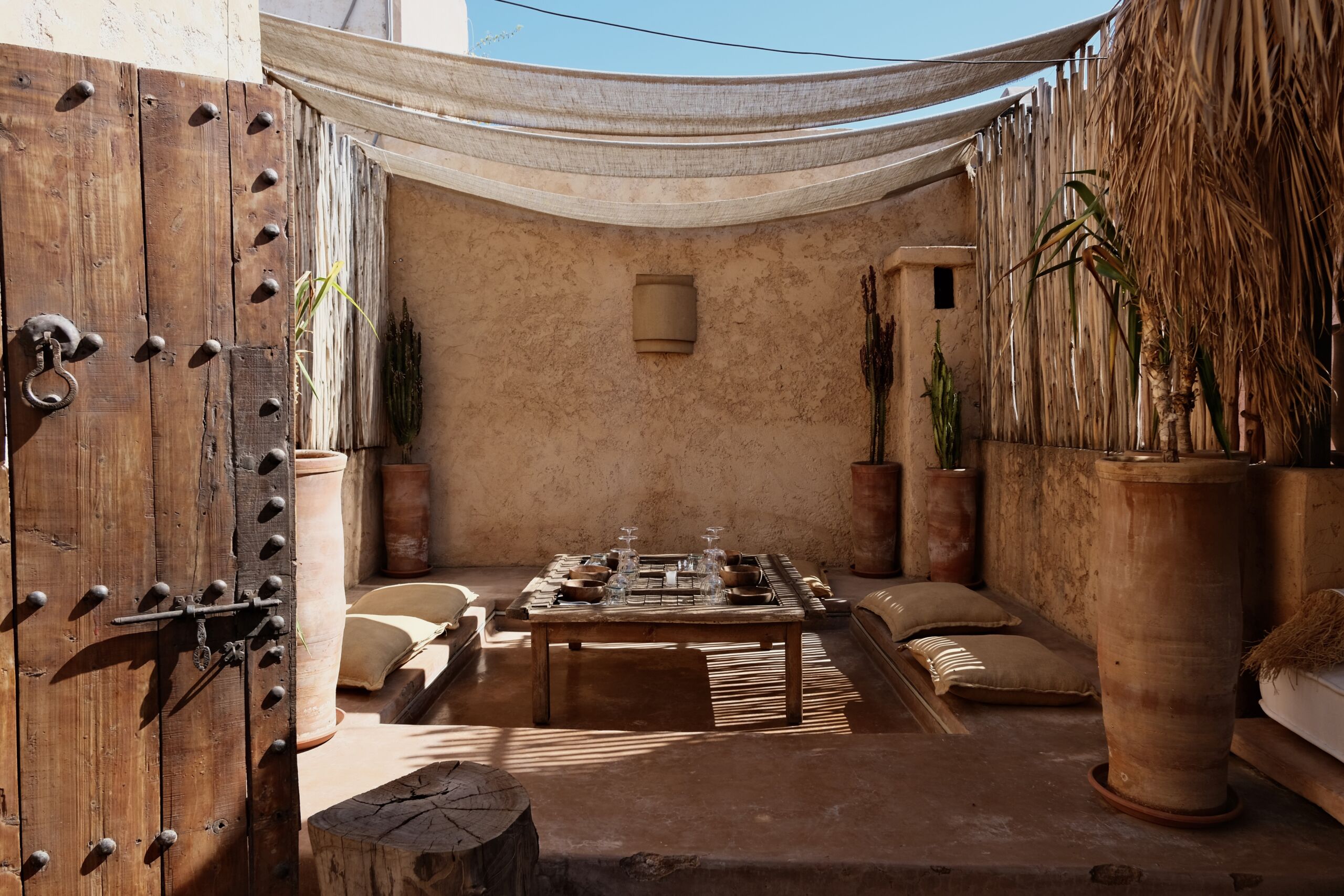 Patio ombragé d'AZULIK I INLA, restaurant de la médina de Marrakech : table dressée sous un voile, porte en bois ancienne
